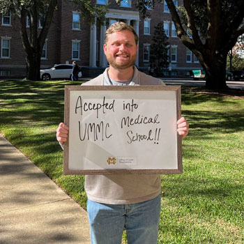 Mason Kennedy proudly holding a med school acceptance sign